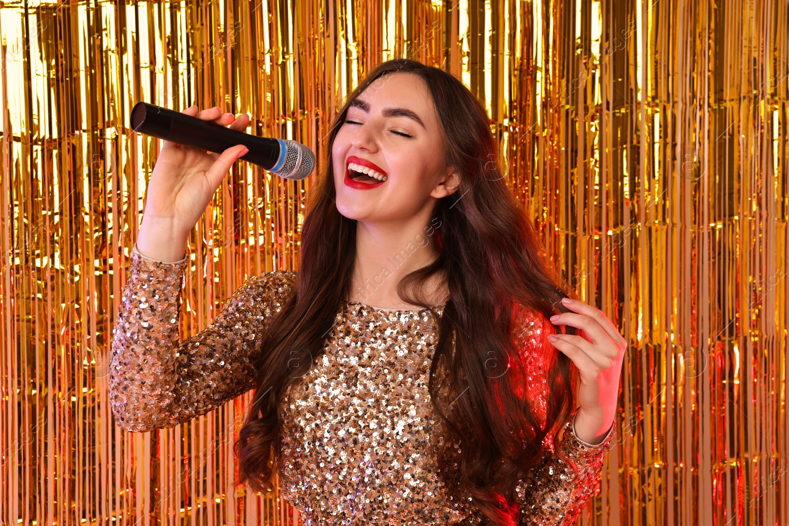 Photo of Young woman with microphone singing against foil curtain