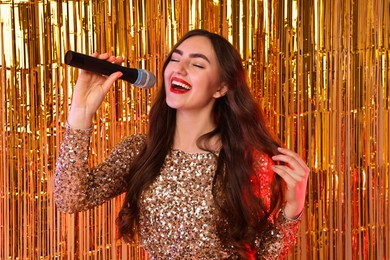 Photo of Young woman with microphone singing against foil curtain