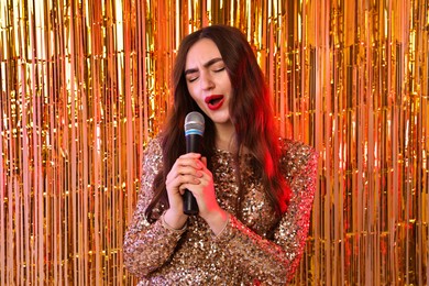 Photo of Young woman with microphone singing against foil curtain