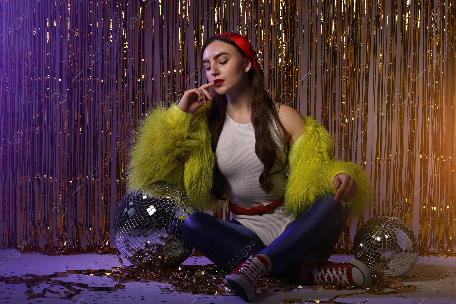 Photo of Beautiful young woman in retro outfit with shiny tinsel and disco balls indoors