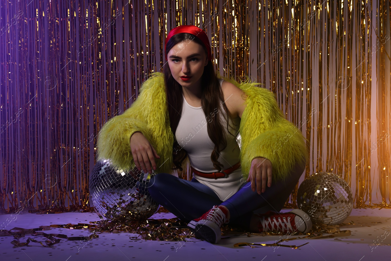 Photo of Beautiful young woman in retro outfit with shiny tinsel and disco balls indoors