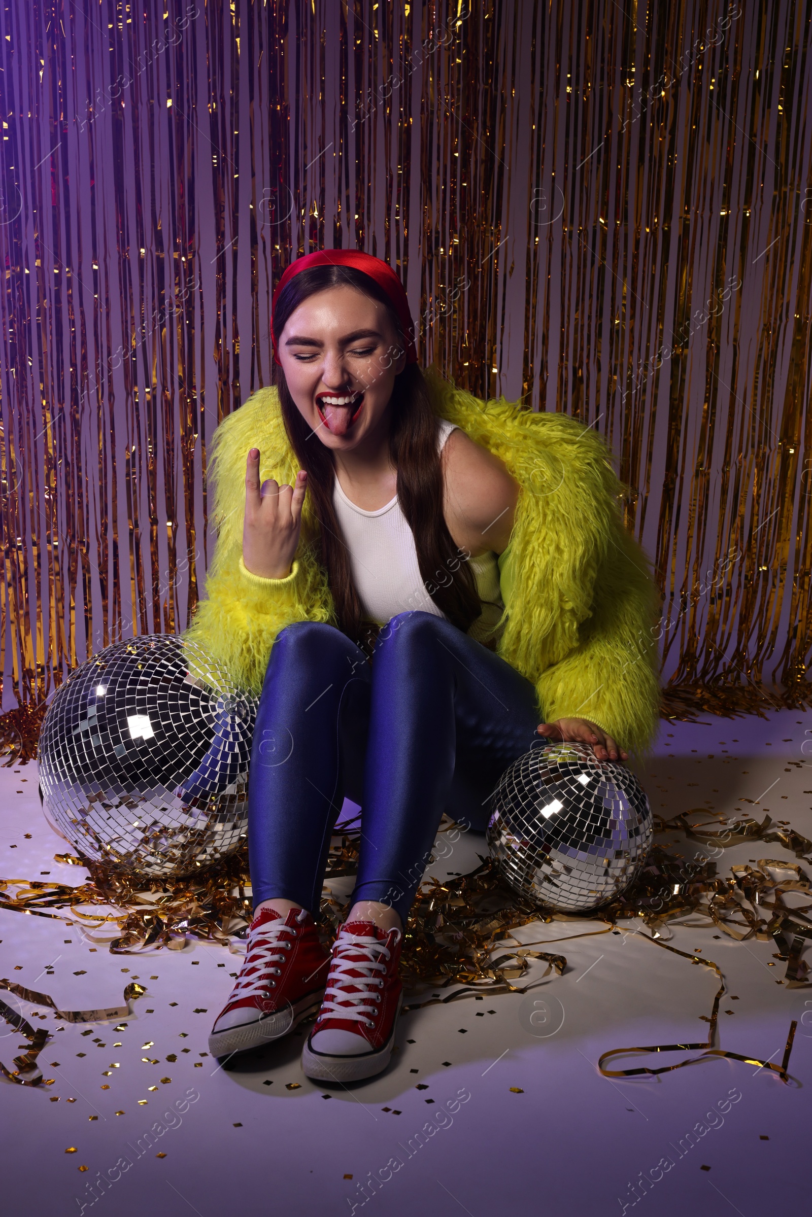 Photo of Emotional young woman in retro outfit with shiny tinsel and disco balls indoors