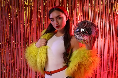 Photo of Beautiful young woman in faux fur coat with disco ball against golden foil curtain