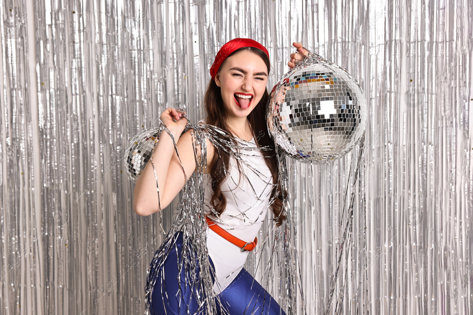 Photo of Beautiful young woman in retro outfit with disco balls against silver foil curtain