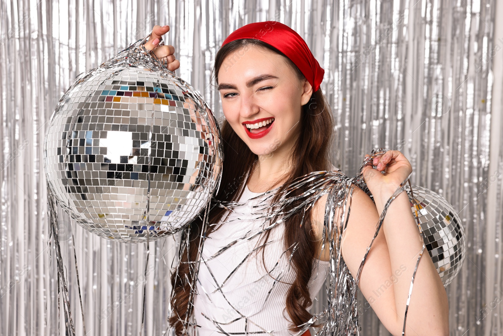 Photo of Beautiful young woman with disco balls against silver foil curtain