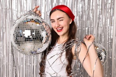 Photo of Beautiful young woman with disco balls against silver foil curtain