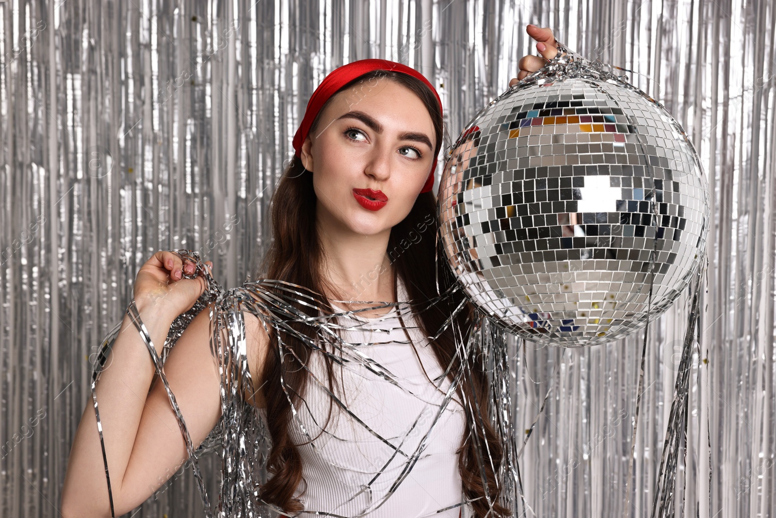 Photo of Beautiful young woman with disco balls against silver foil curtain