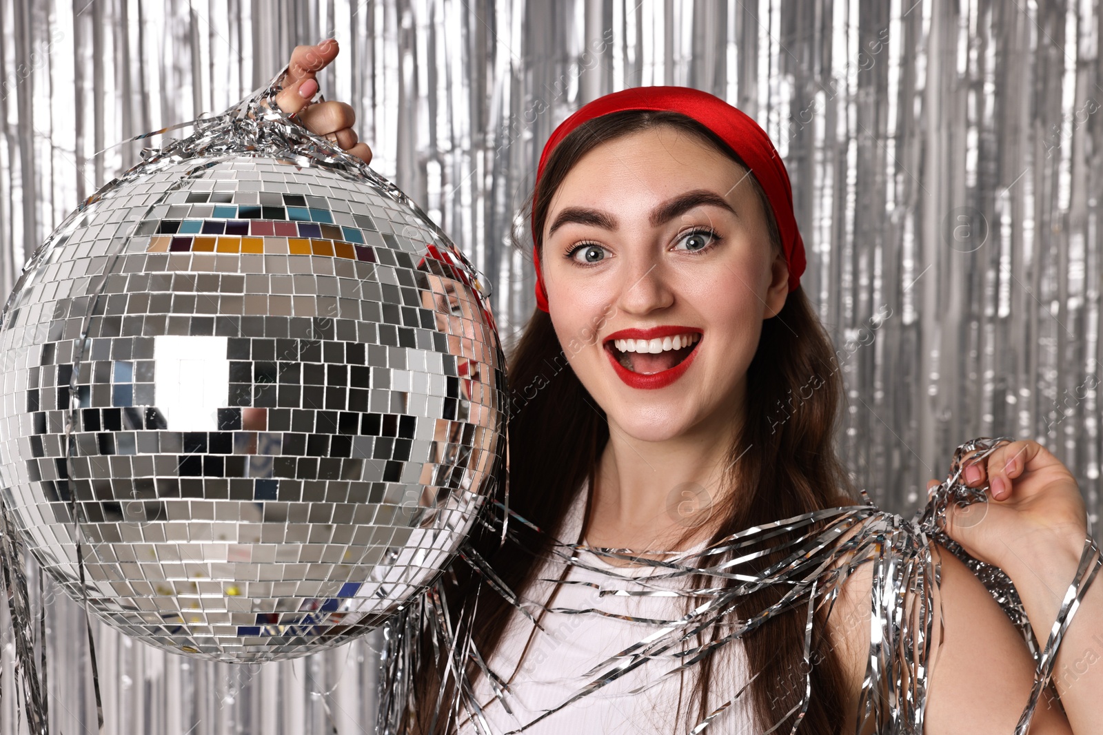 Photo of Beautiful young woman with disco ball against silver foil curtain