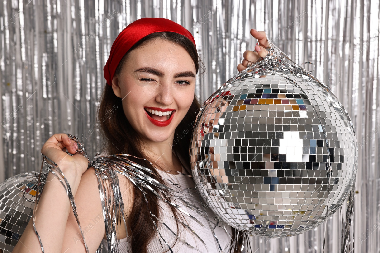 Photo of Beautiful young woman with disco balls against silver foil curtain