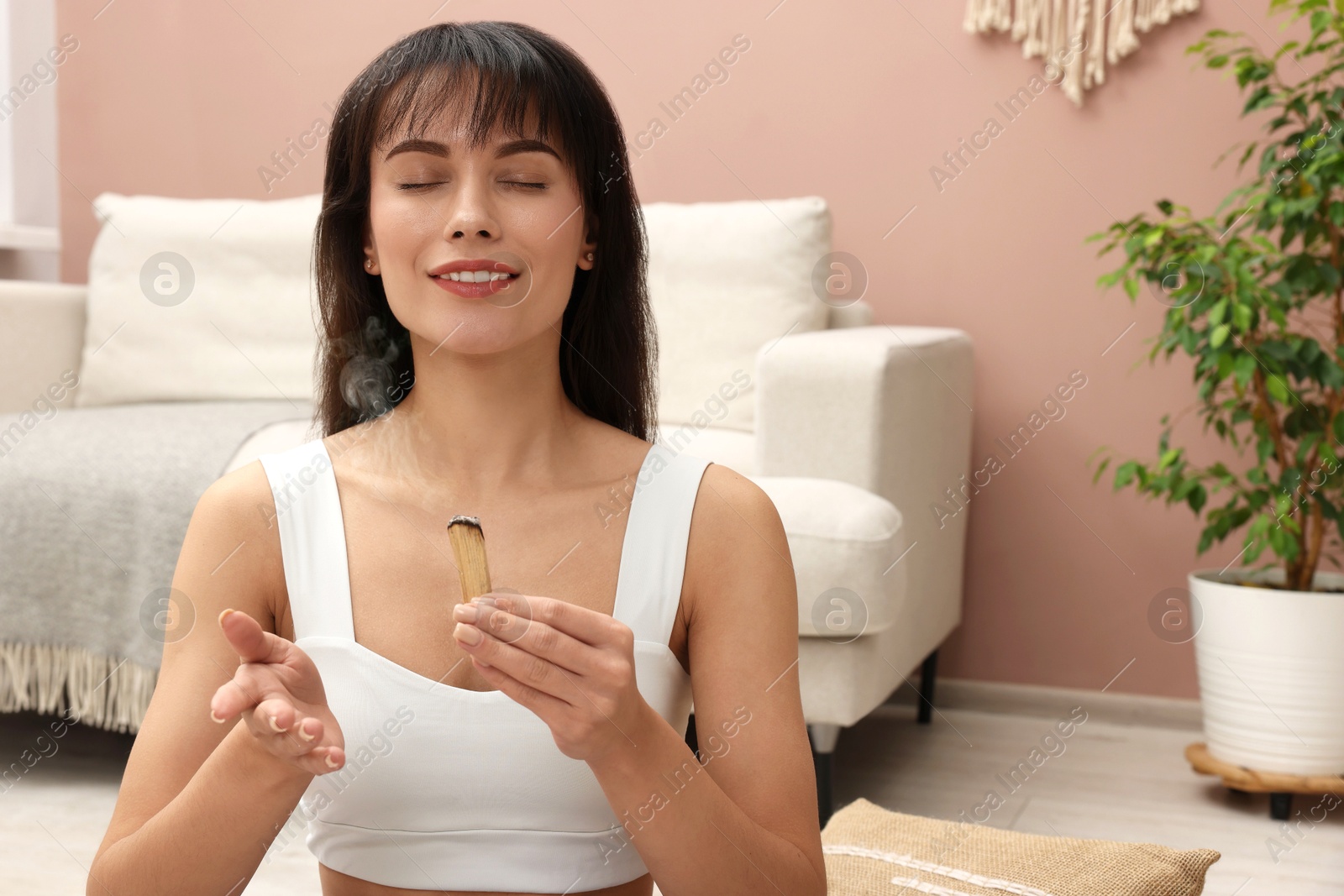 Photo of Woman with smoldering palo santo stick at home, space for text