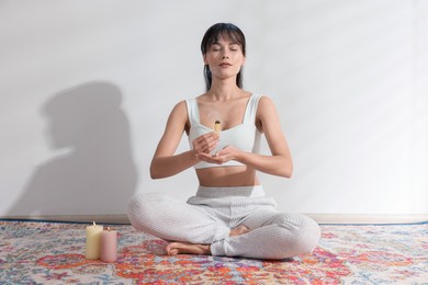 Photo of Woman with smoldering palo santo stick on floor at home