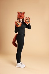 Photo of Quadrobics. Girl wearing fox mask, gloves and tail on beige background