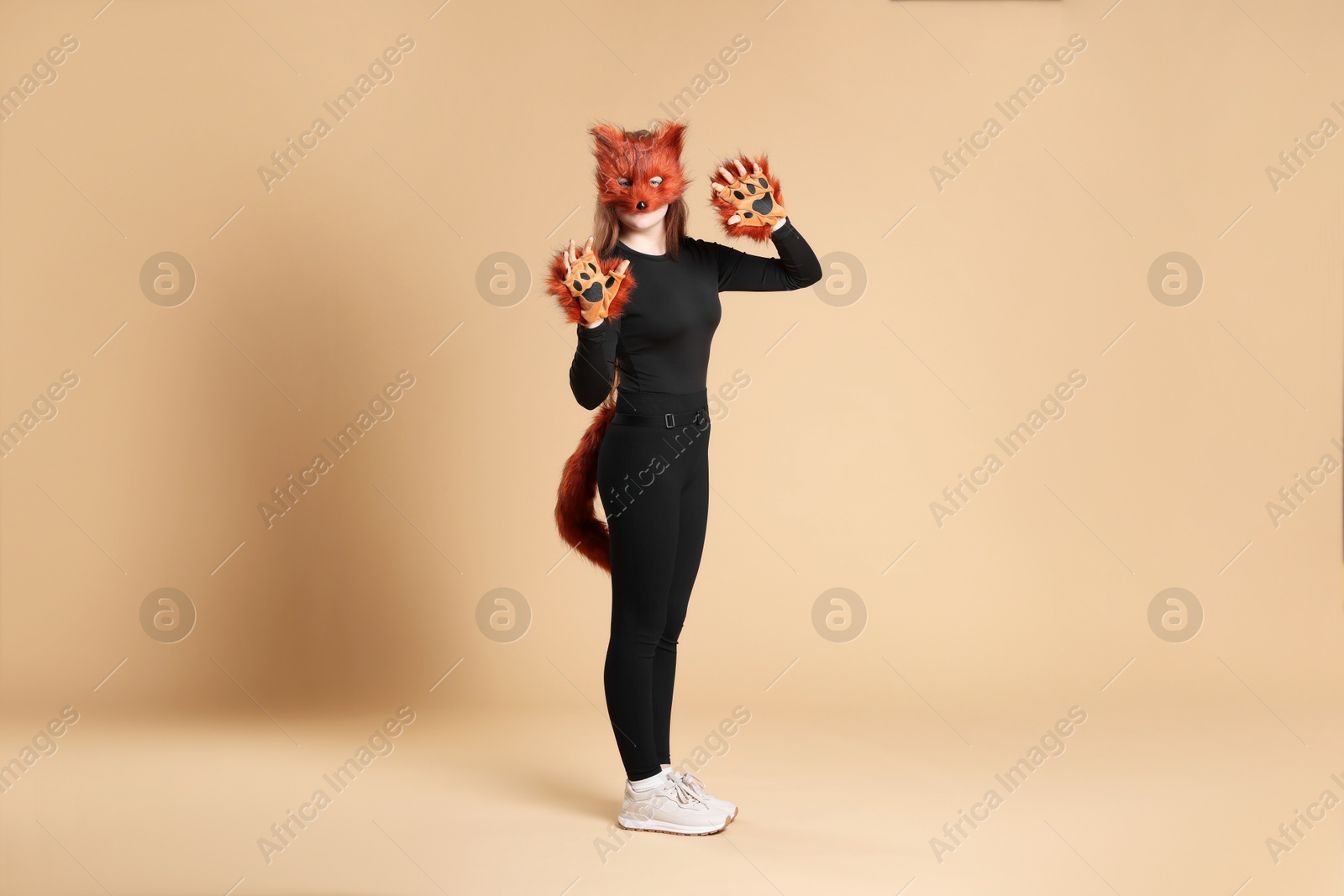 Photo of Quadrobics. Girl wearing fox mask, gloves and tail on beige background