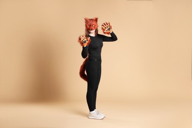 Photo of Quadrobics. Girl wearing fox mask, gloves and tail on beige background