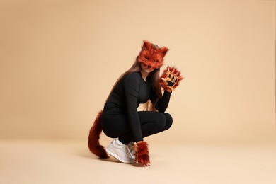 Photo of Quadrobics. Girl wearing fox mask, gloves and tail on beige background