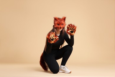 Photo of Quadrobics. Girl wearing fox mask, gloves and tail on beige background