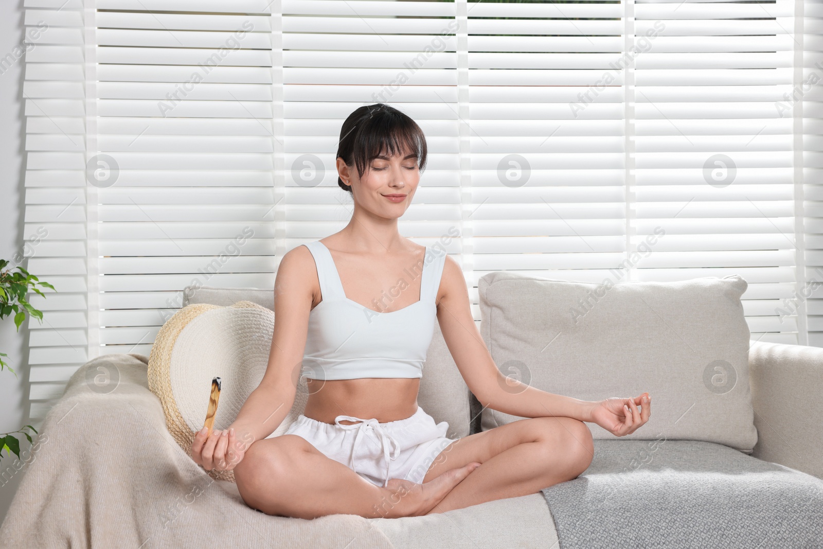 Photo of Woman with palo santo stick meditating on sofa at home