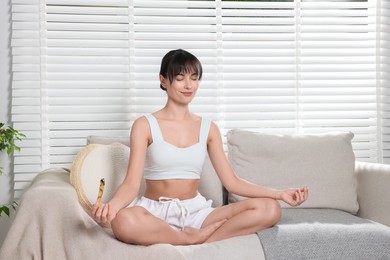 Photo of Woman with palo santo stick meditating on sofa at home