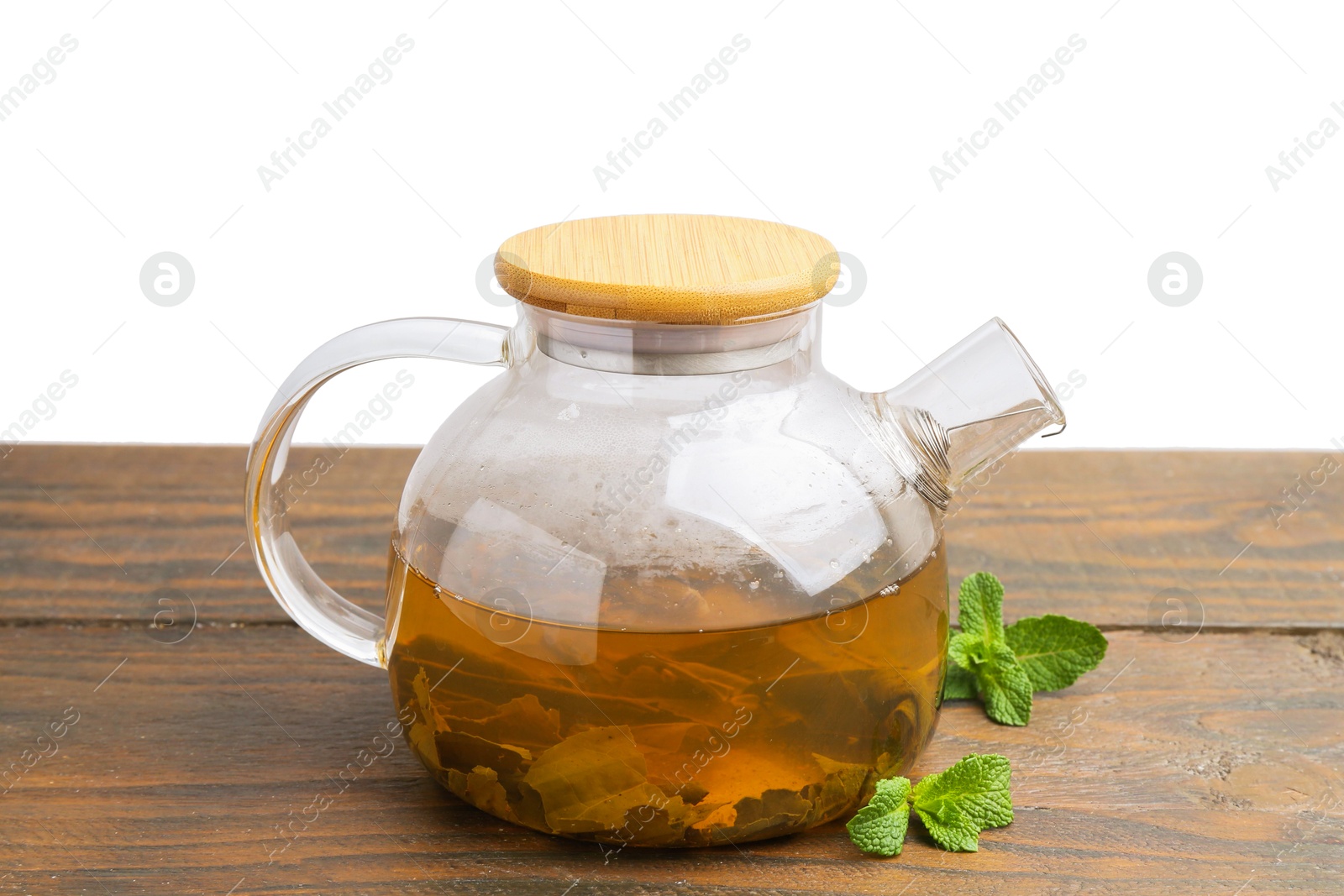 Photo of Aromatic mint tea in glass teapot and fresh leaves on wooden table against white background