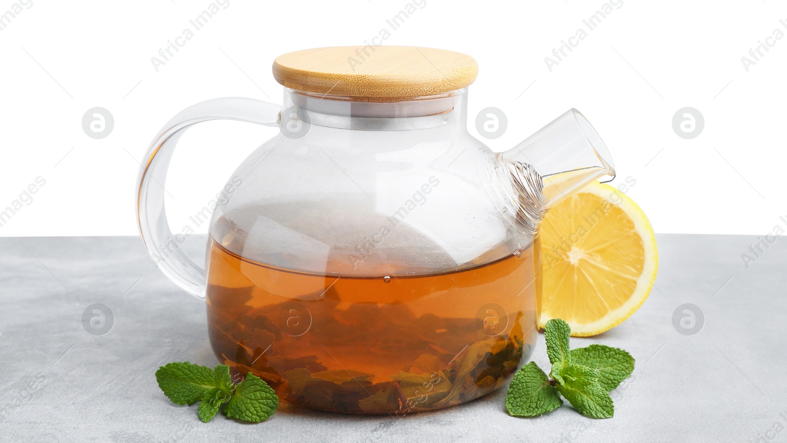 Photo of Aromatic mint tea in glass teapot, fresh leaves and lemon on light gray table against white background