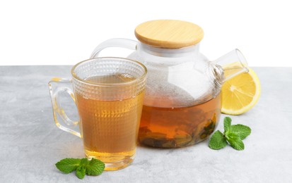 Photo of Aromatic mint tea, fresh leaves and lemon on light gray table against white background