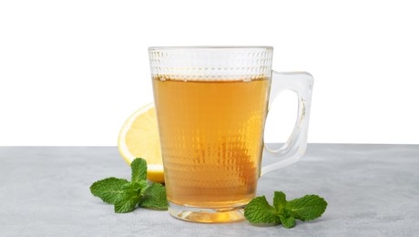 Photo of Aromatic mint tea in glass cup, fresh leaves and lemon on light gray table against white background