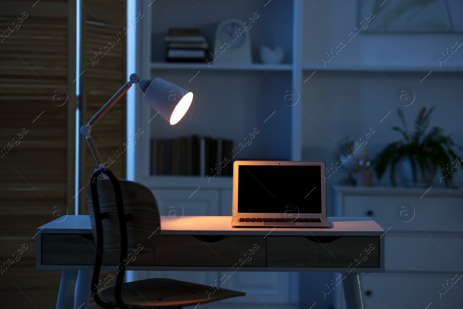 Photo of Comfortable workplace with laptop and lamp on table indoors