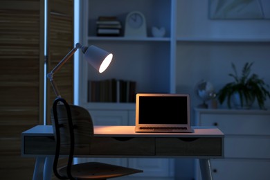 Photo of Comfortable workplace with laptop and lamp on table indoors