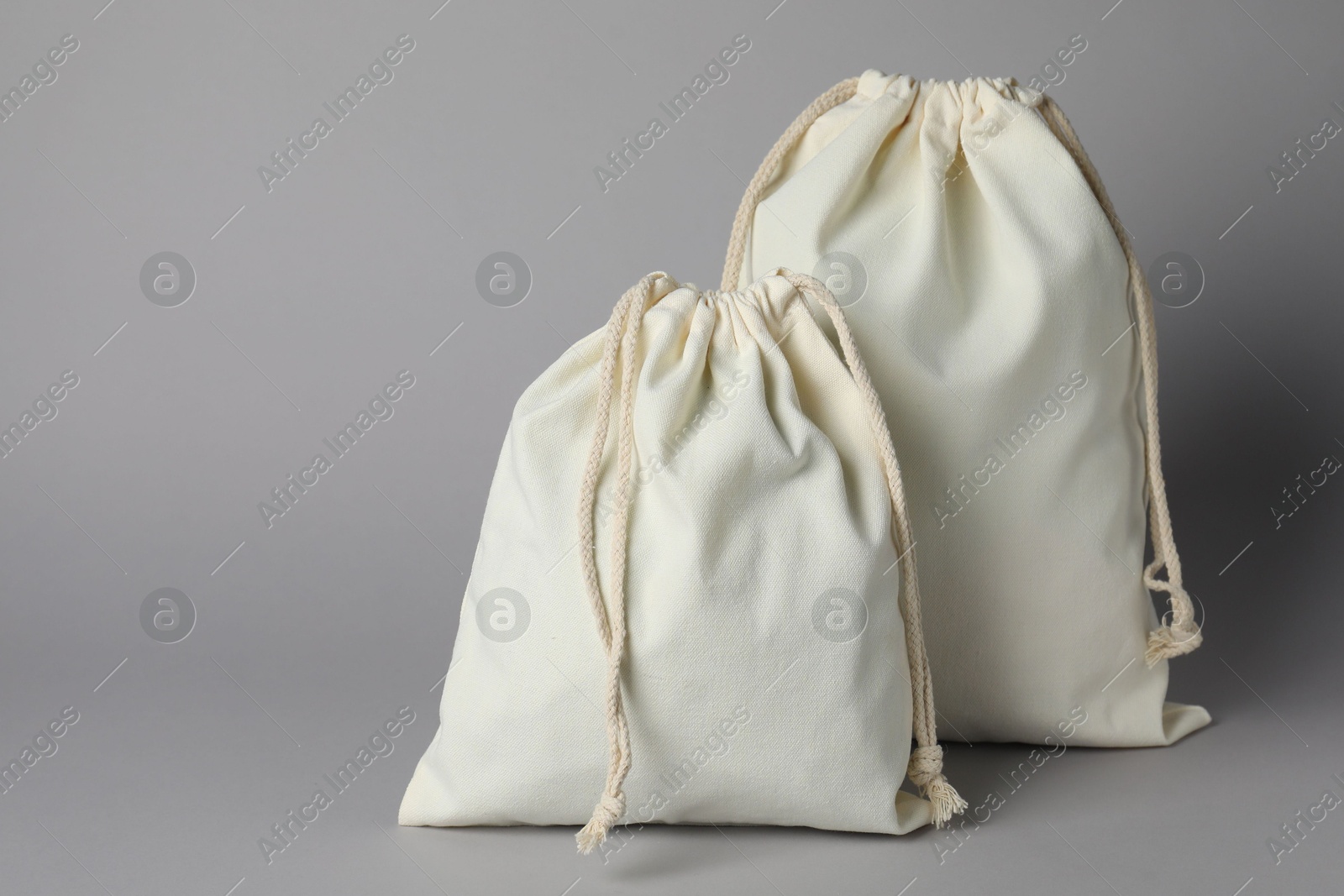 Photo of White cotton bags with ties on grey background. Space for text