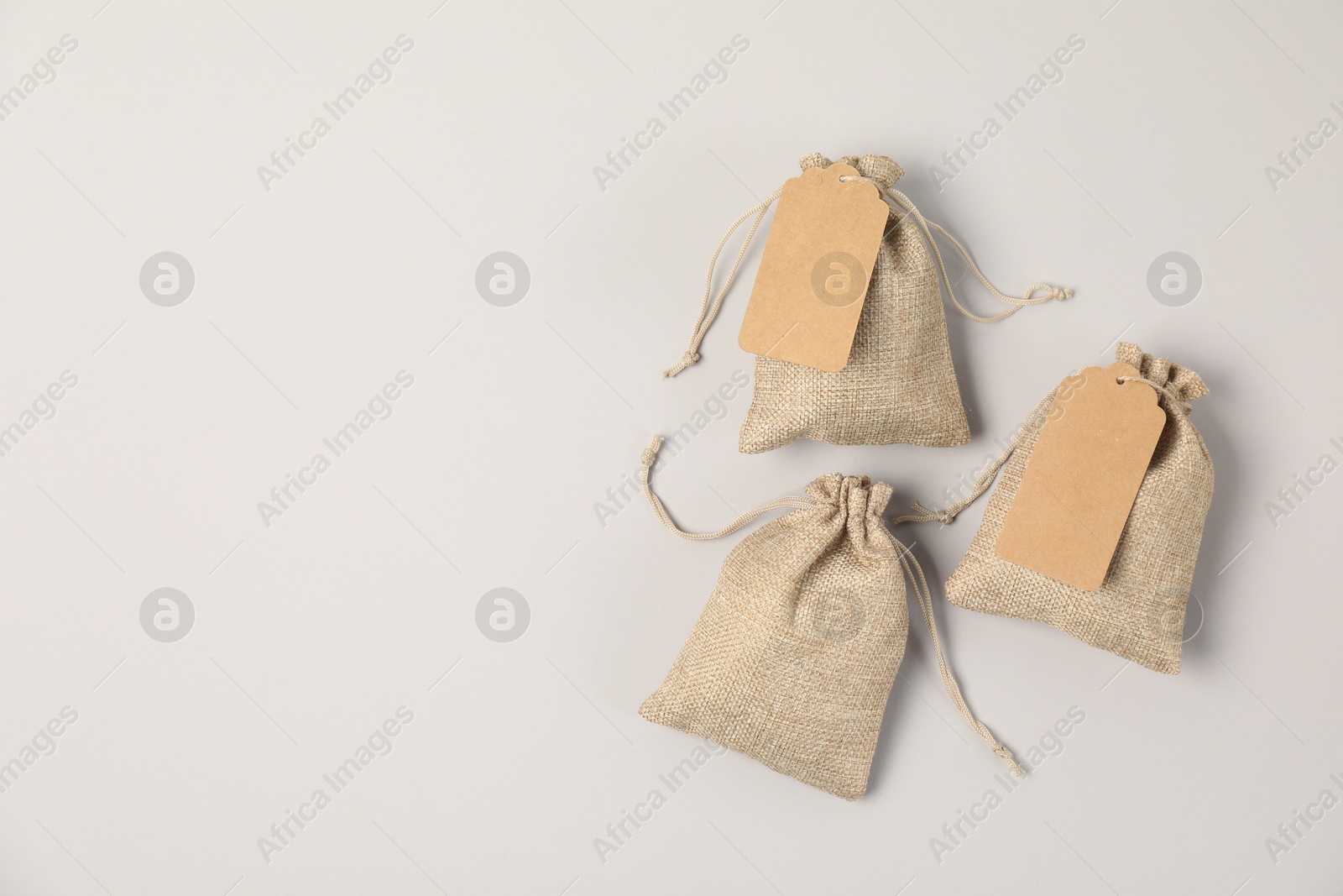 Photo of Burlap bags with tags on light grey background, flat lay. Space for text