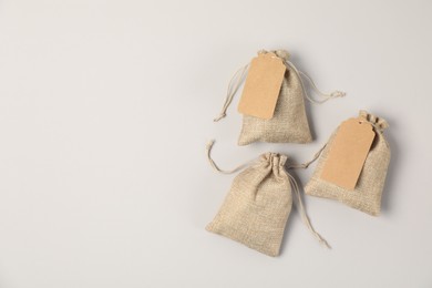 Burlap bags with tags on light grey background, flat lay. Space for text