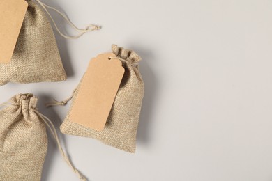 Burlap bags with tags on light grey background, flat lay. Space for text