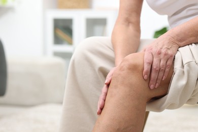 Photo of Woman suffering from pain in her knee at home, closeup. Space for text