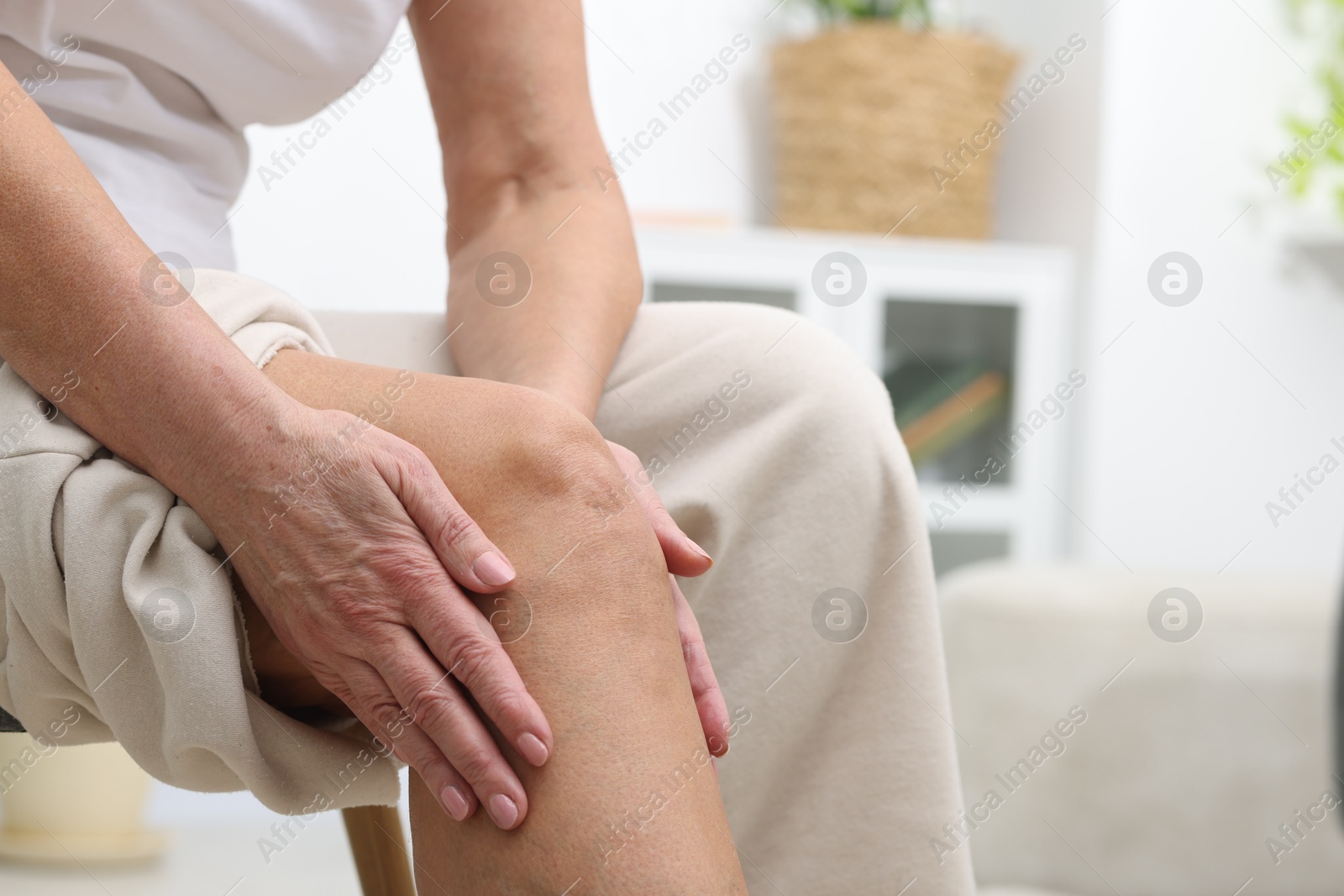 Photo of Woman suffering from pain in her knee at home, closeup. Space for text