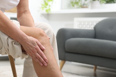 Photo of Woman suffering from pain in her knee at home, closeup. Space for text