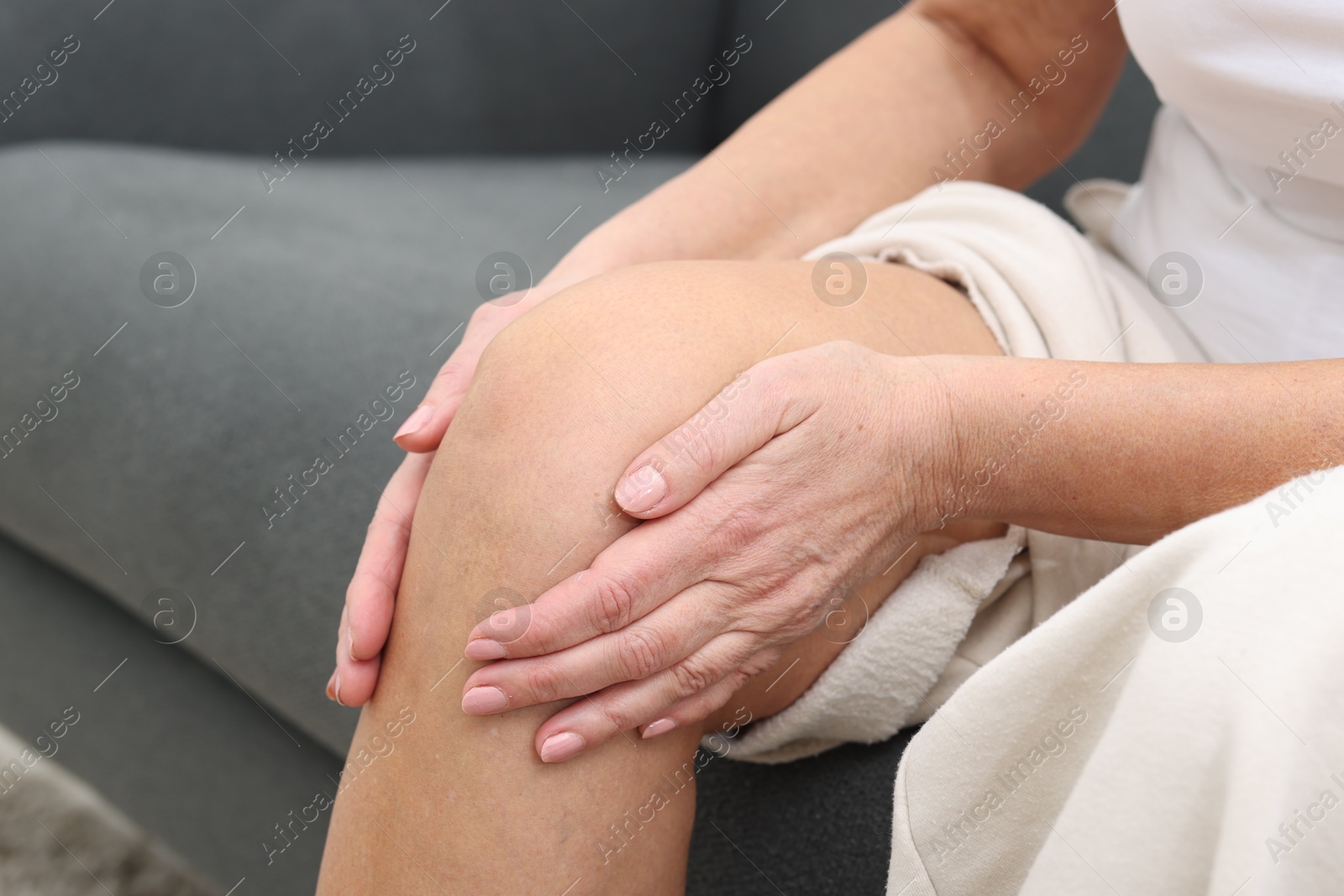 Photo of Woman suffering from pain in her knee on sofa, closeup