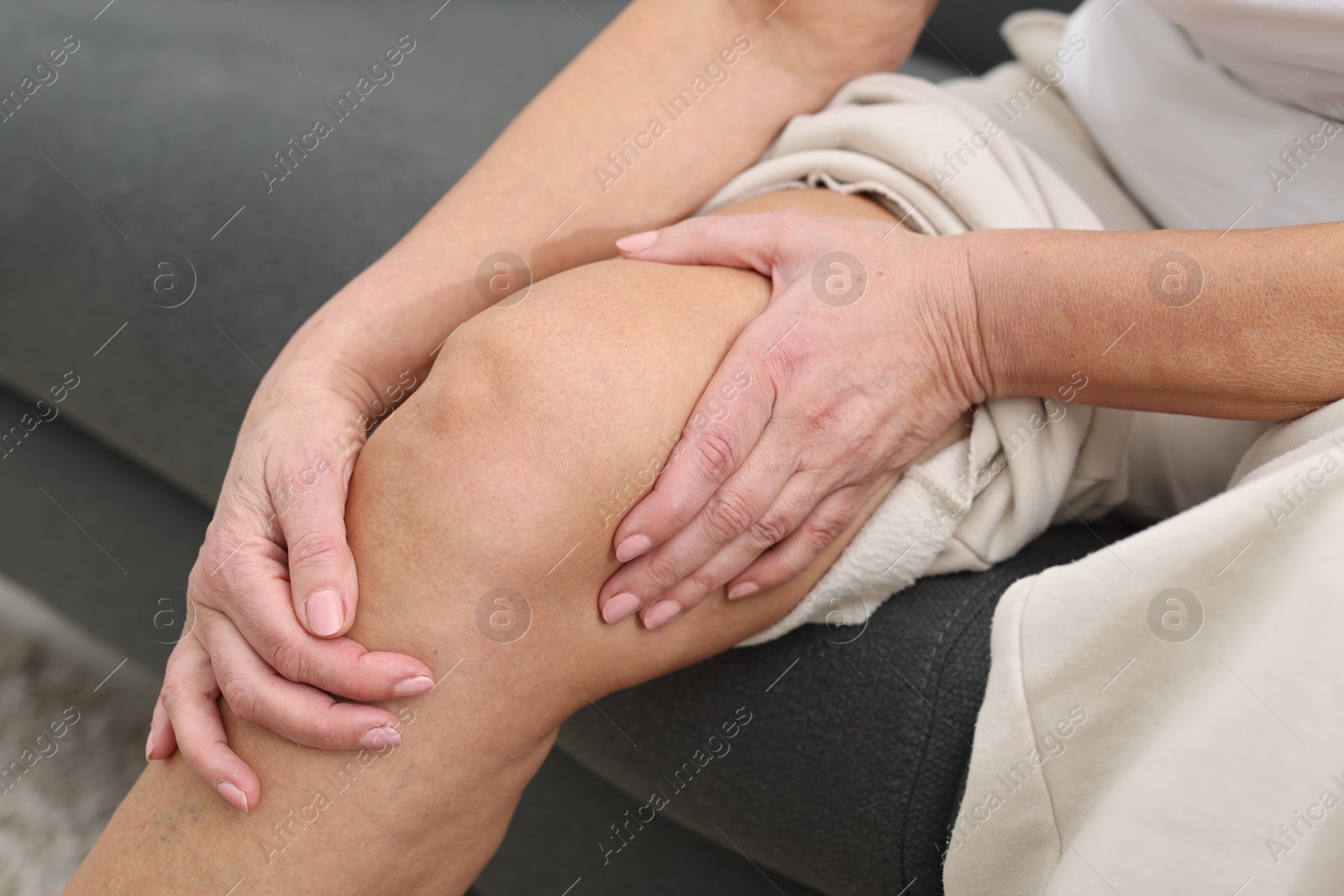 Photo of Woman suffering from pain in her knee on sofa, closeup