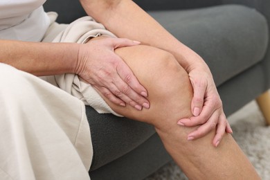 Photo of Woman suffering from pain in her knee on sofa, closeup