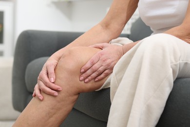 Photo of Woman suffering from pain in her knee on sofa indoors, closeup