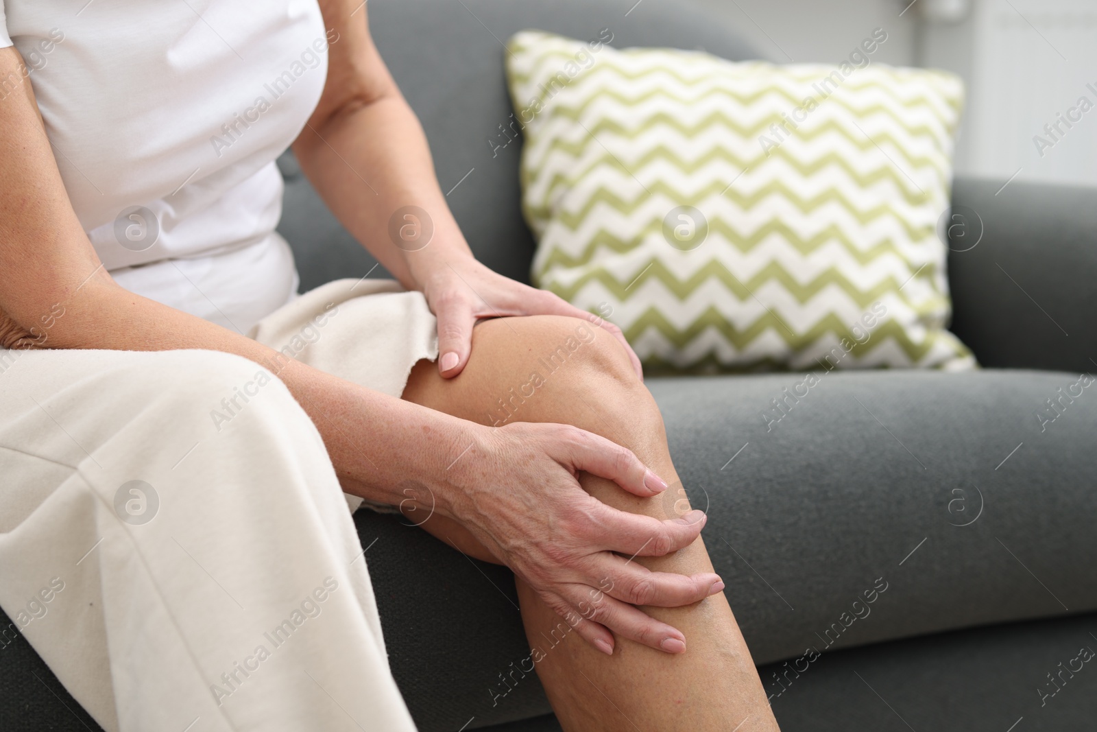 Photo of Woman suffering from pain in her knee on sofa, closeup