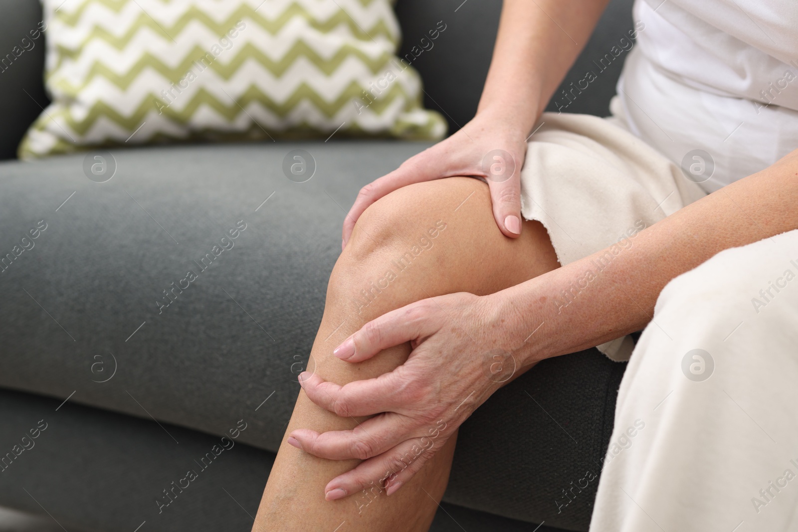 Photo of Woman suffering from pain in her knee on sofa, closeup