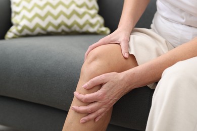 Photo of Woman suffering from pain in her knee on sofa, closeup