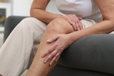 Photo of Woman suffering from pain in her knee on sofa indoors, closeup