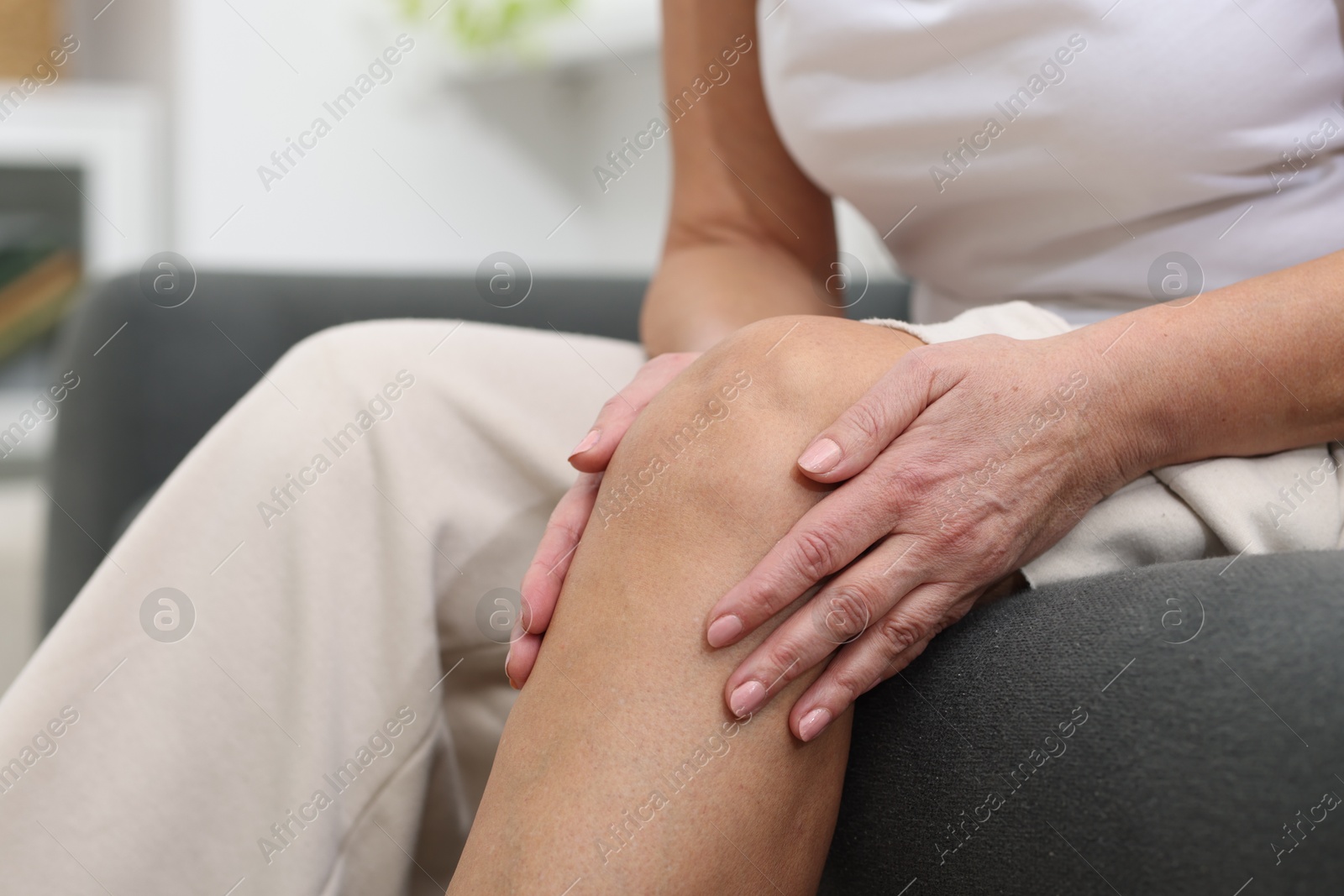 Photo of Woman suffering from pain in her knee on sofa indoors, closeup