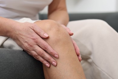 Photo of Woman suffering from pain in her knee on sofa indoors, closeup