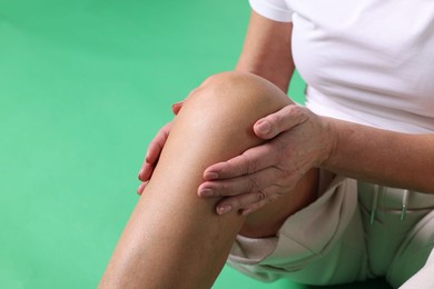 Photo of Woman suffering from pain in her knee on green background, closeup