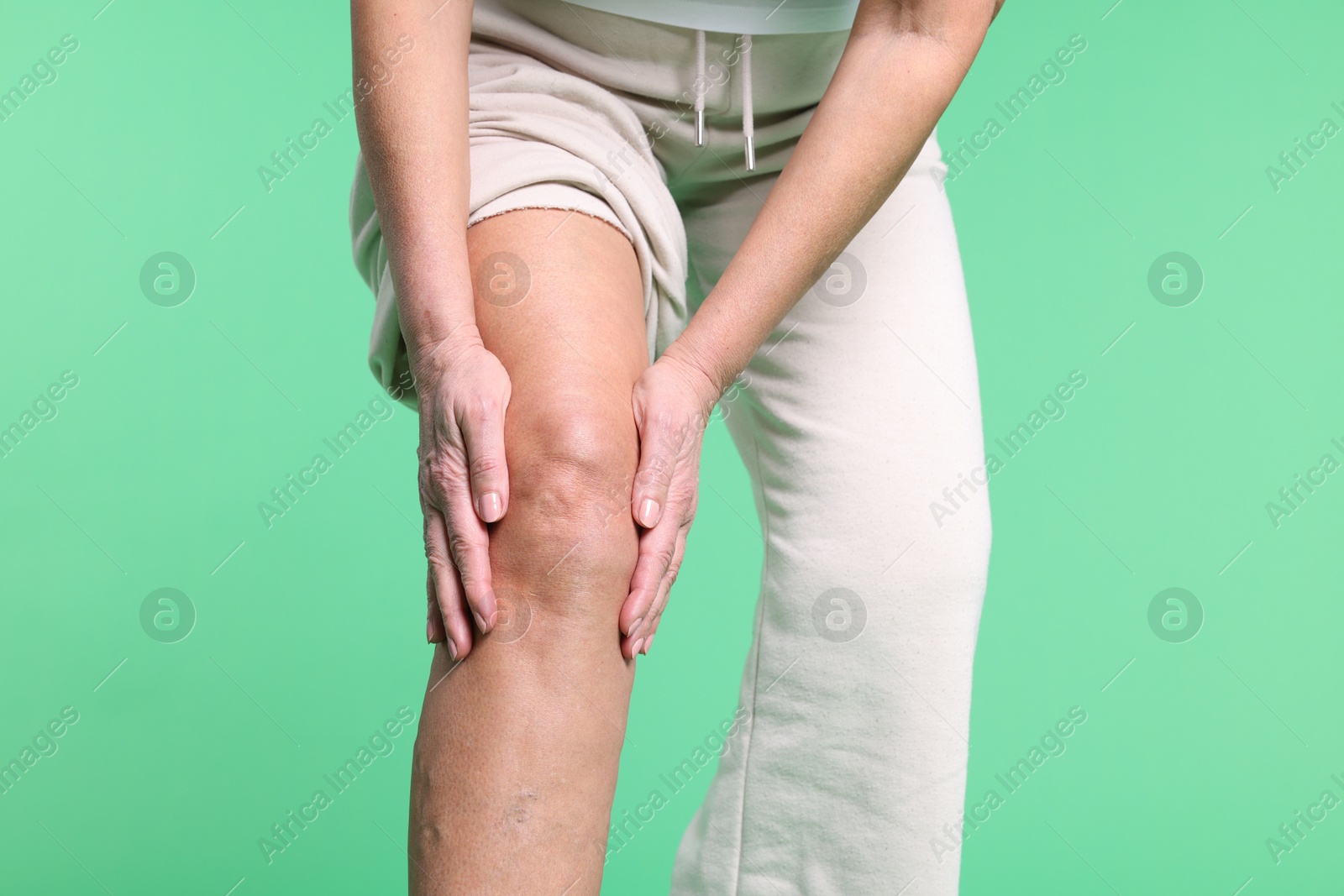 Photo of Woman suffering from pain in her knee on green background, closeup