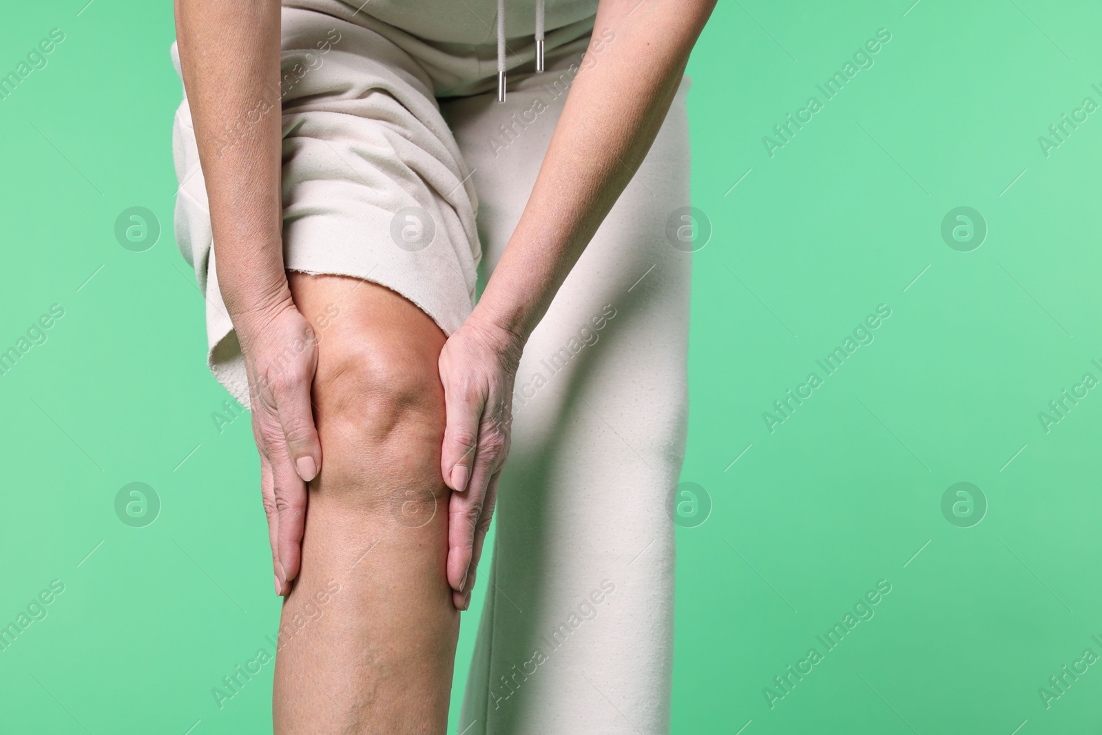 Photo of Woman suffering from pain in her knee on green background, closeup