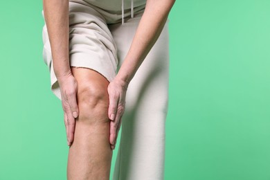 Photo of Woman suffering from pain in her knee on green background, closeup