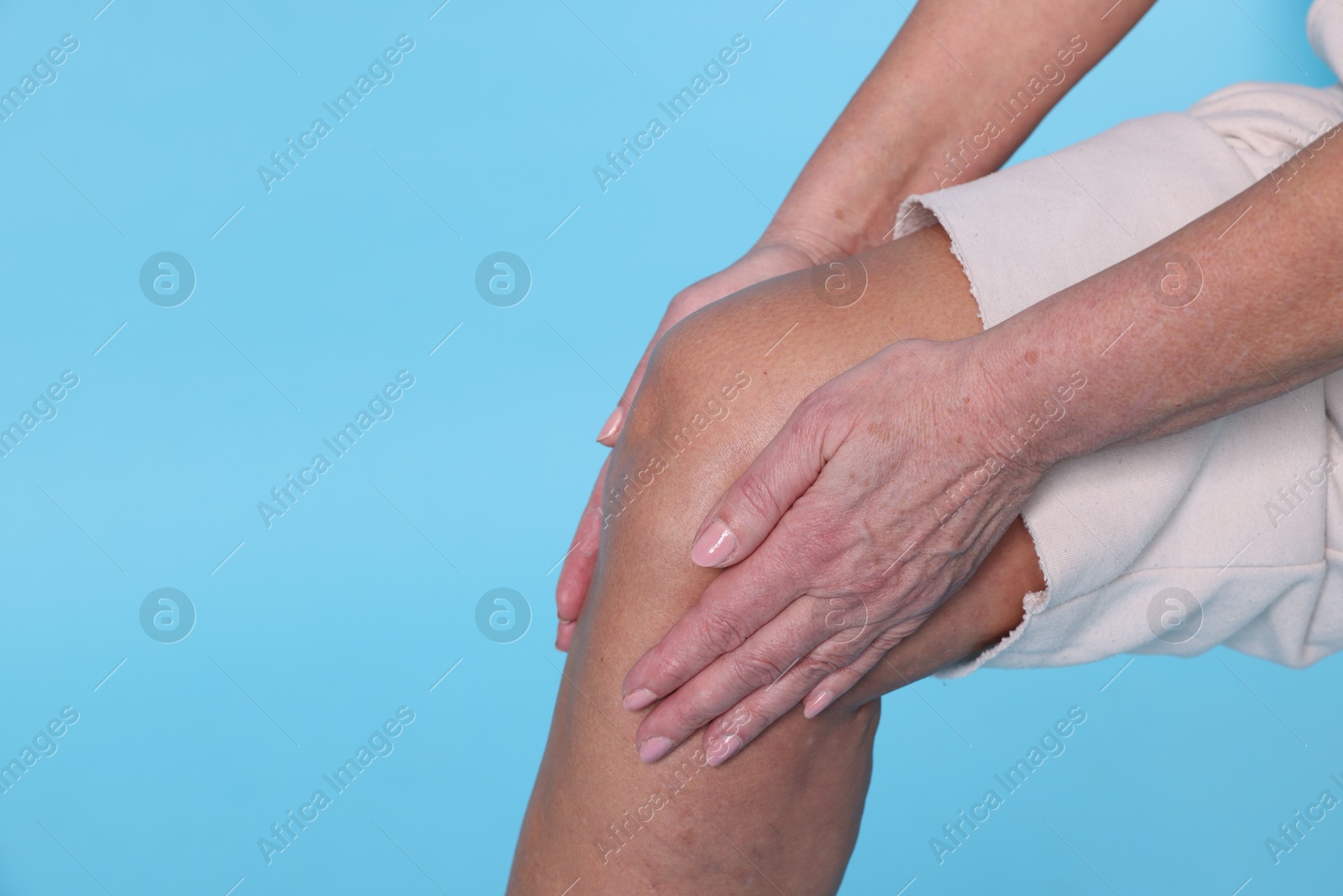 Photo of Woman suffering from pain in her knee on light blue background, closeup. Space for text